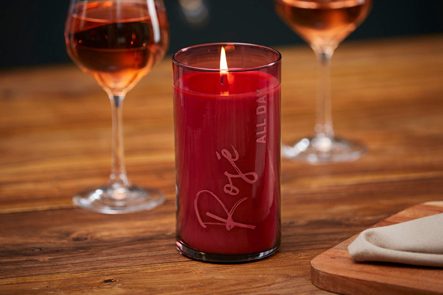 Red candle labeled 'Rosé' with two glasses of rosé wine on a wooden table.