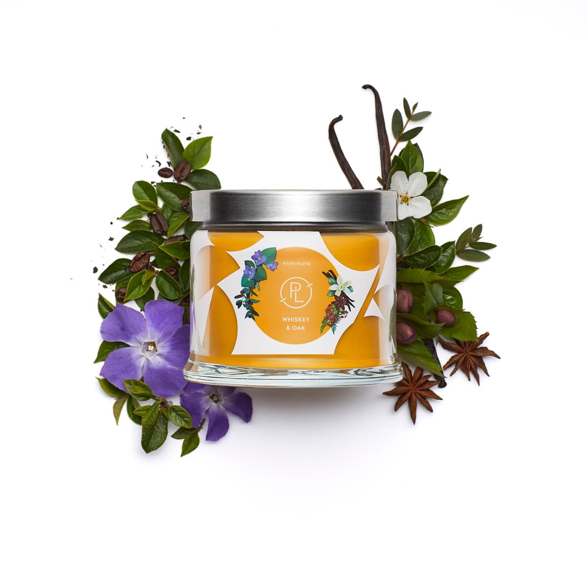 Whiskey & Oak 3-wick jar candle surrounded by leaves and a flowers against a white background.