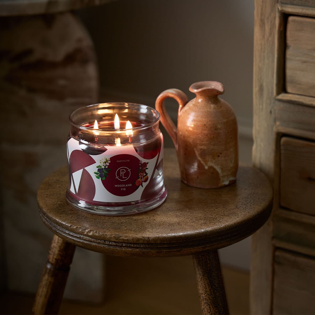 Woodland Fig 3-Wick Jar Candle lit on a small wooden table.