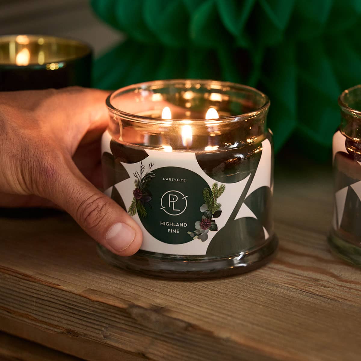 Highland Pine 3-wick jar candle shown lit on a wooden surface.