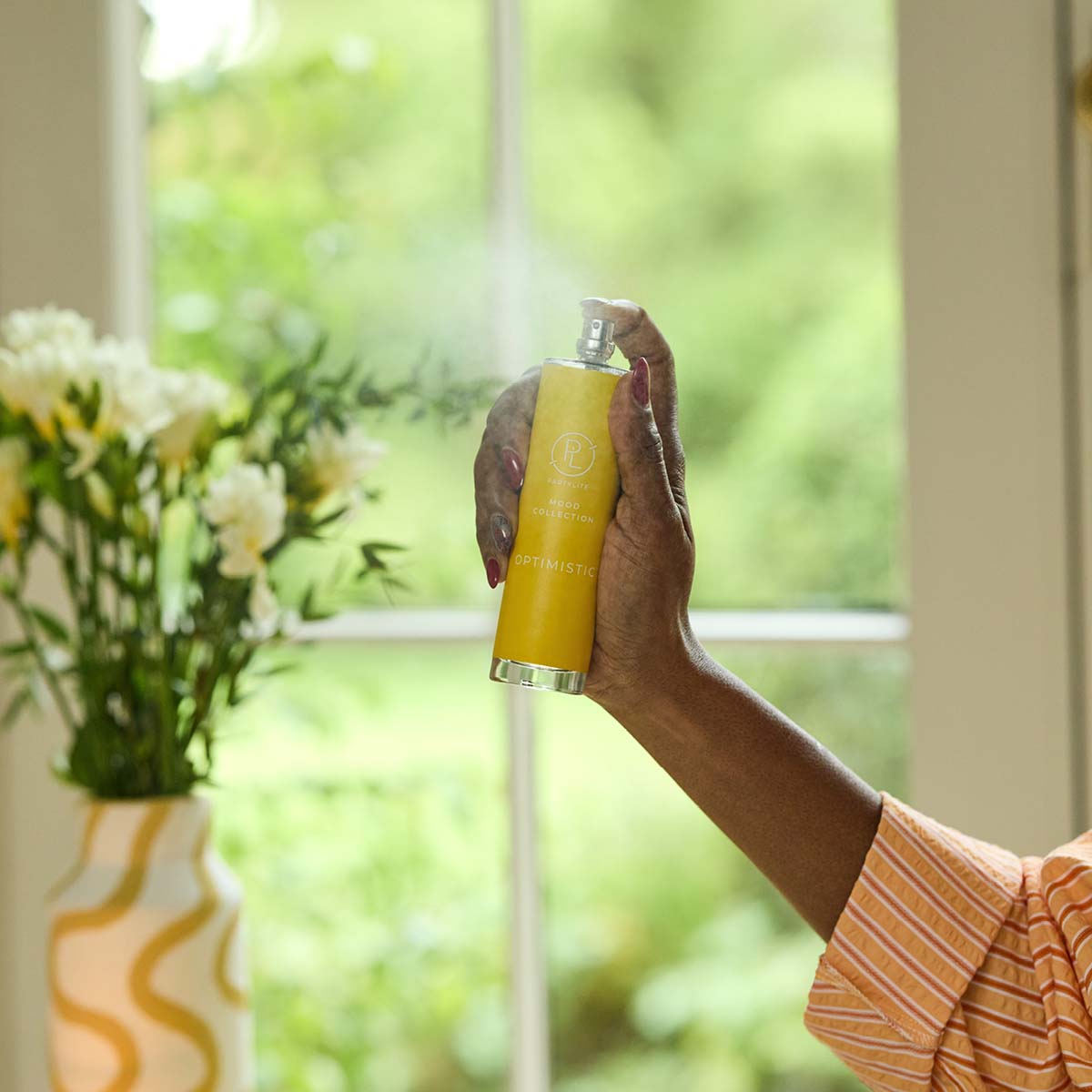 Optimistic Room Spray being shown used with a vase of flowers in the background.