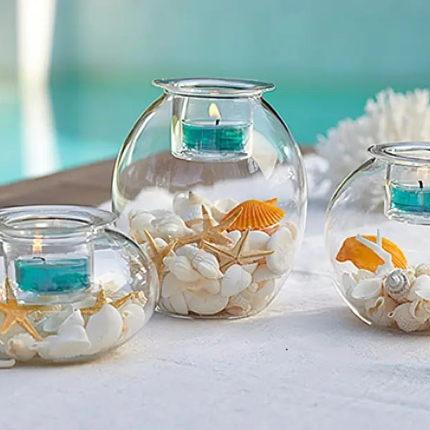 Clearly Creative Tealight Trio with lit tealights, decorative shells and pebbles on a white cloth.