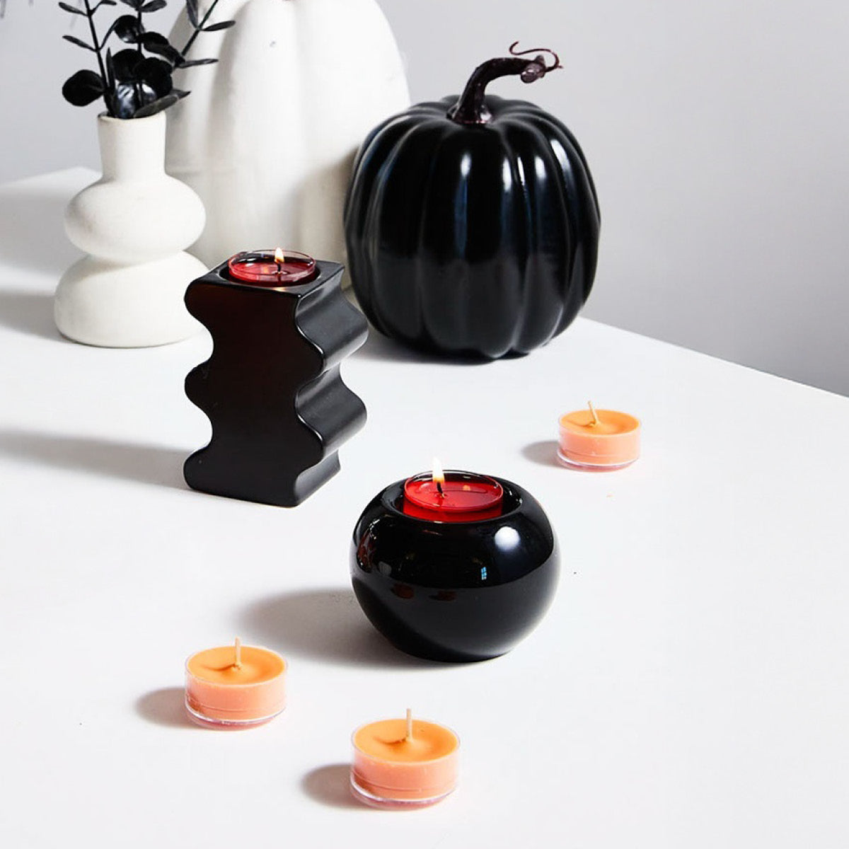 Woodland Pumpkin Tealights shown with black tealight holders with white vase with black leaves on a white surface