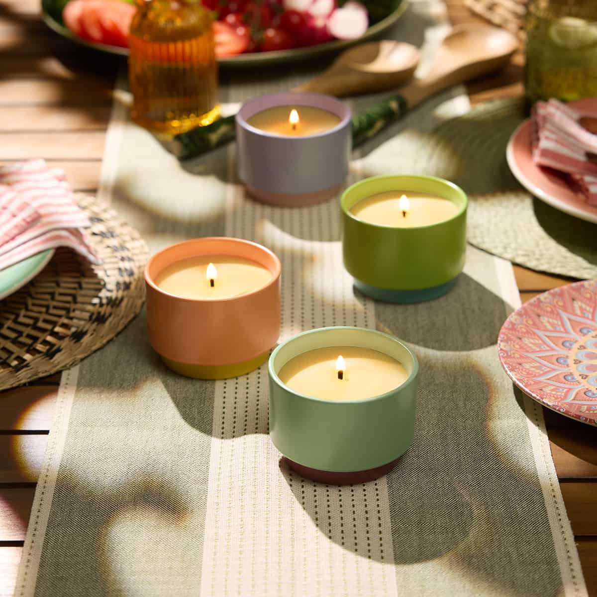 Assortment of Citronella two tone singe wick Jar Candles on a textured green and cream table runner on an wooden table with decorative plates and wooden spoons 