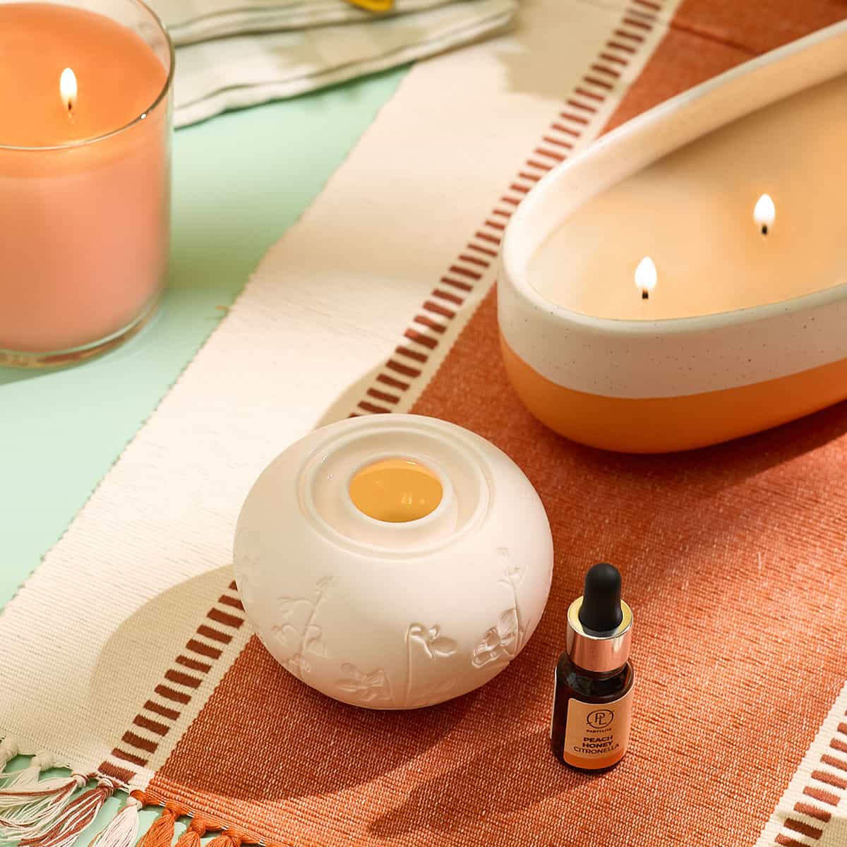 Peach Honey Citronella Fragrance Oil  shown with a Fragrance Warmer and Peach Honey Citronella GloLite Jar and the two tone 4 wick Peach Honey Citronella jar on a woven table mat